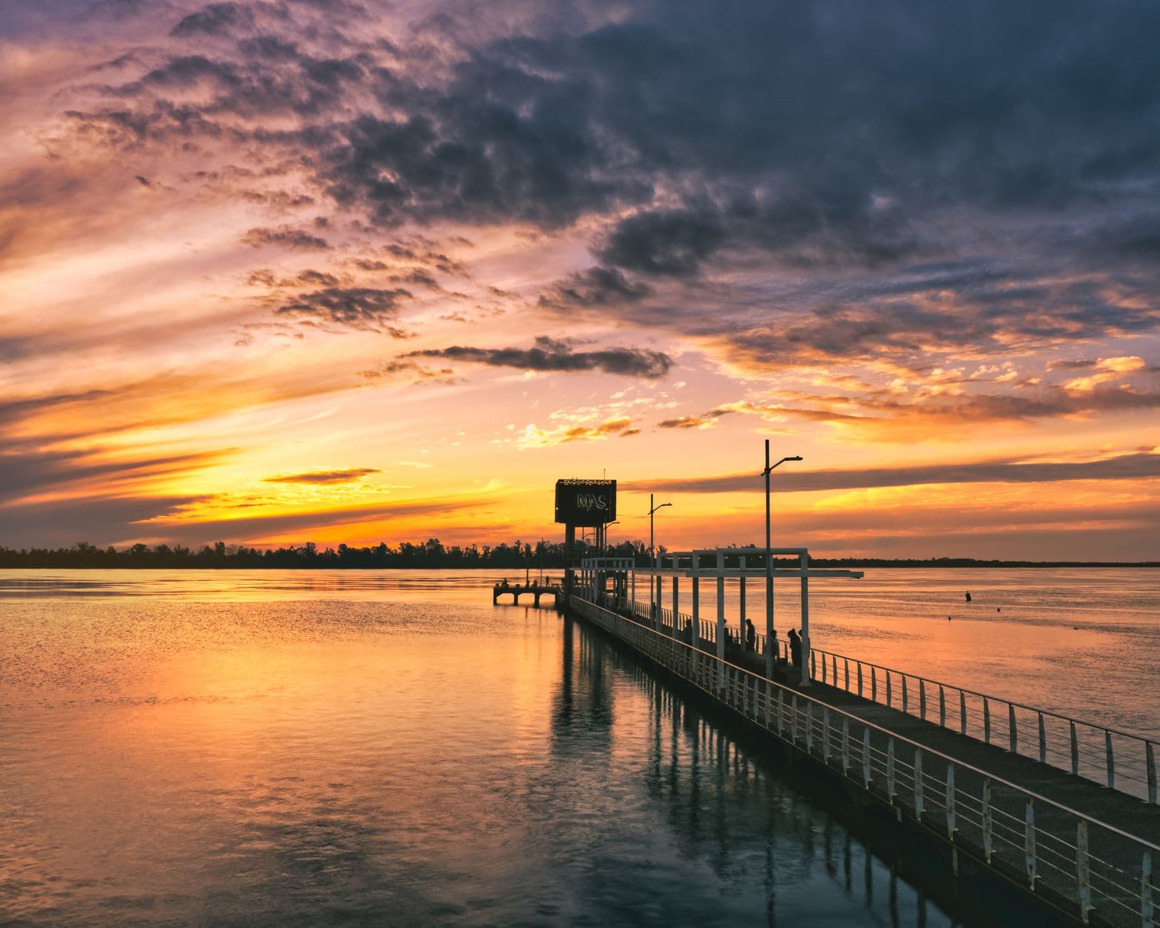 Beautiful sunset reflecting over the water at Paysandú pier, with a vibrant orange sky and clouds.
