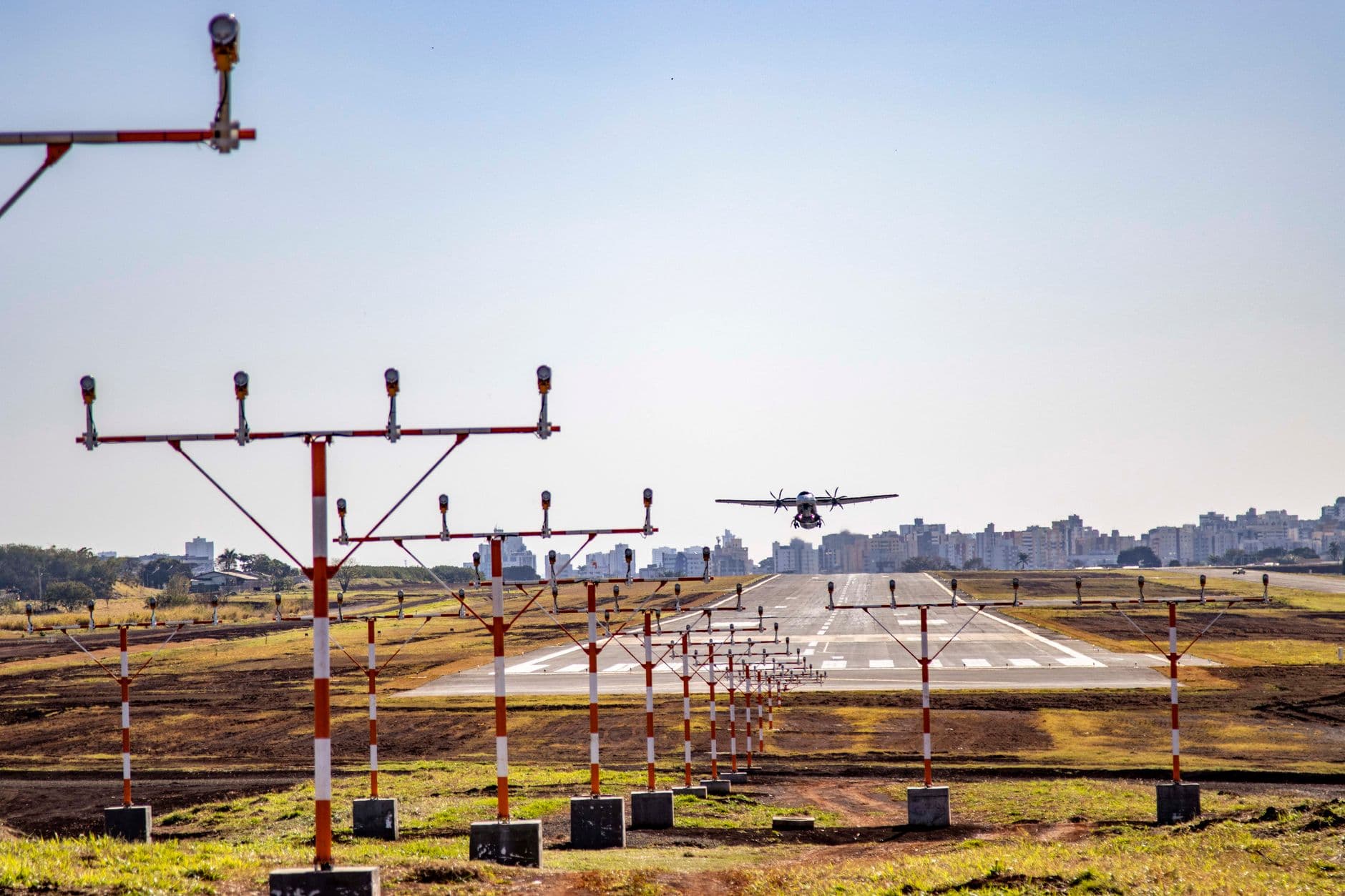 An airplane lands on the runway at Londrina Airport, Brazil, with cityscape in background.