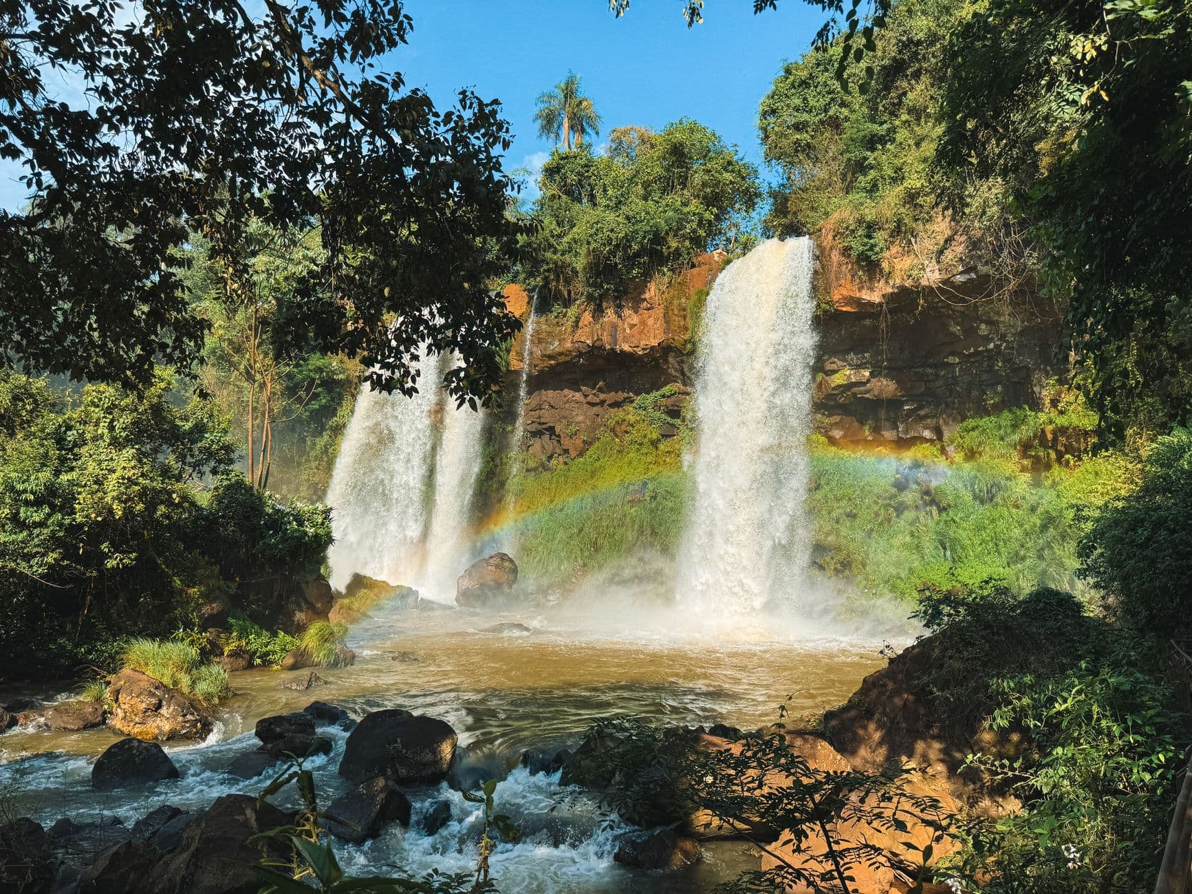 Stunning view of Iguazu Falls in Argentina with a vibrant rainbow and lush greenery.