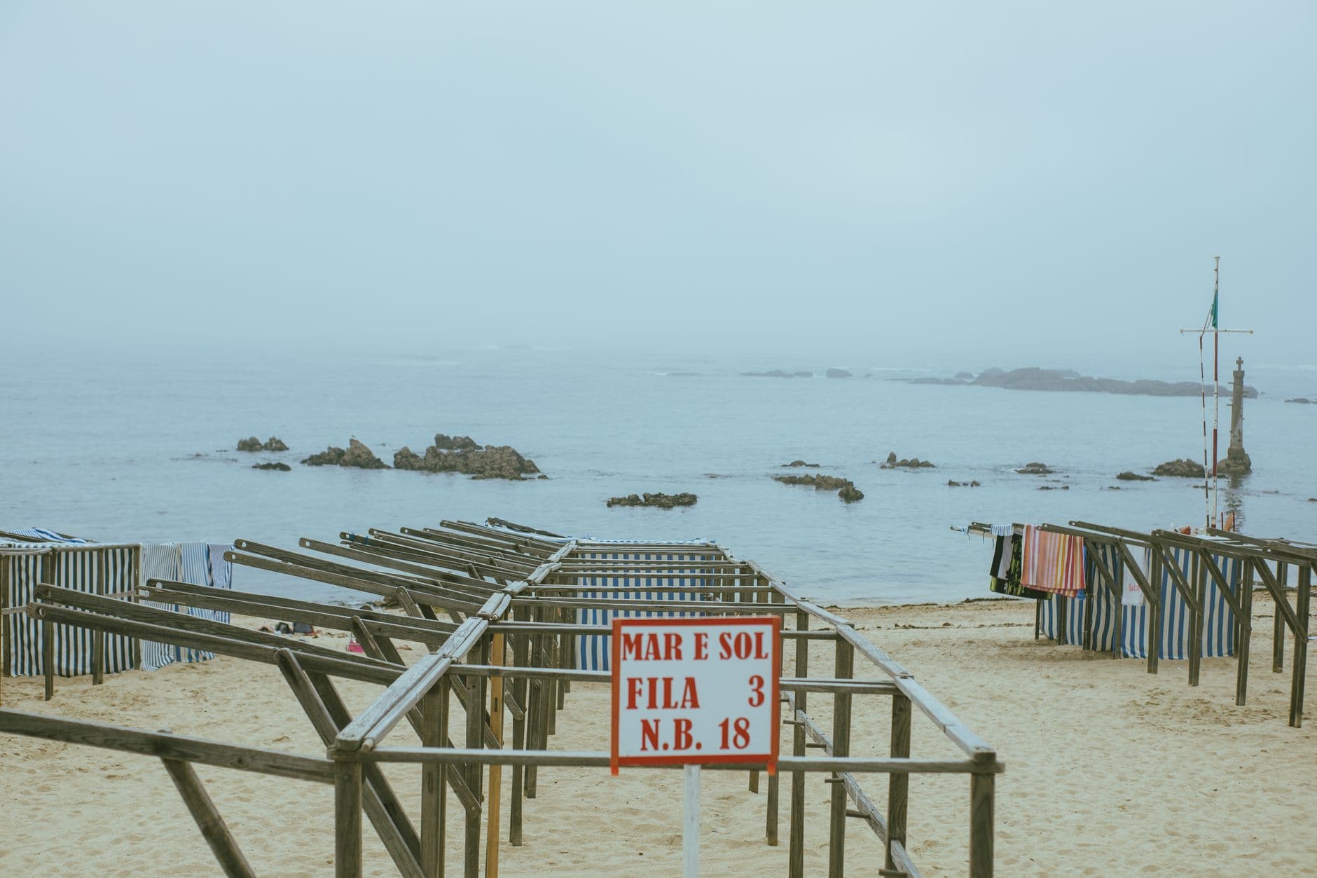 Tranquil foggy beach scene featuring wooden structures and a sign 'MAR E SOL'.