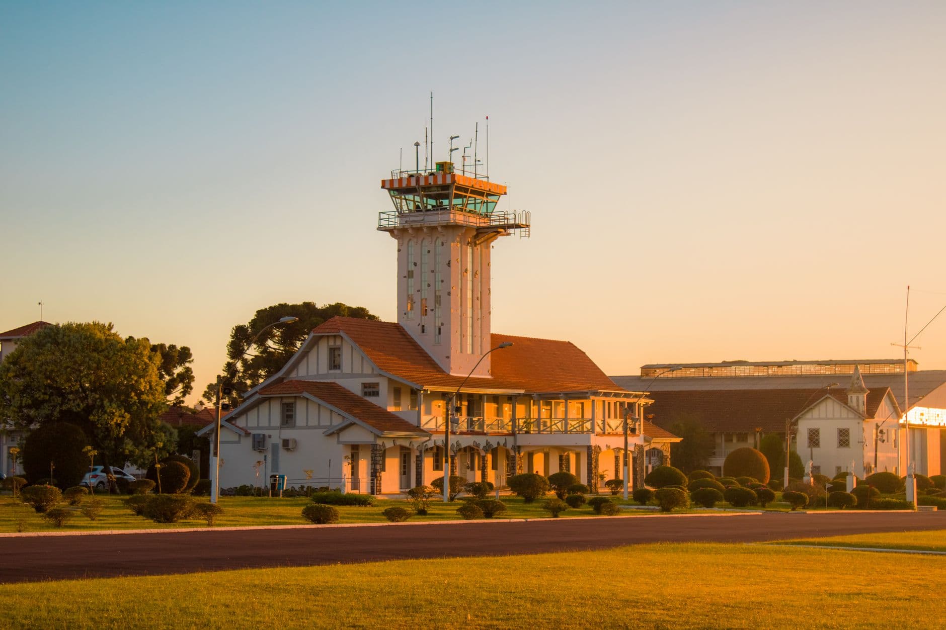 Beautiful sunset view of a historic lighthouse amidst rural buildings and lush greenery.