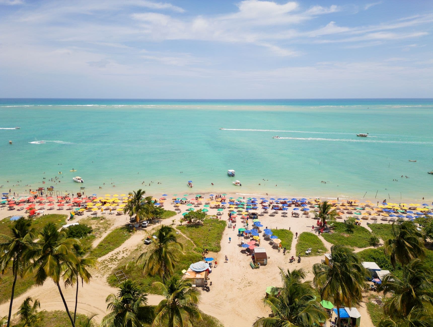 A vibrant aerial view of a tropical beach in Antunes, Brazil, with colorful umbrellas and turquoise waters.