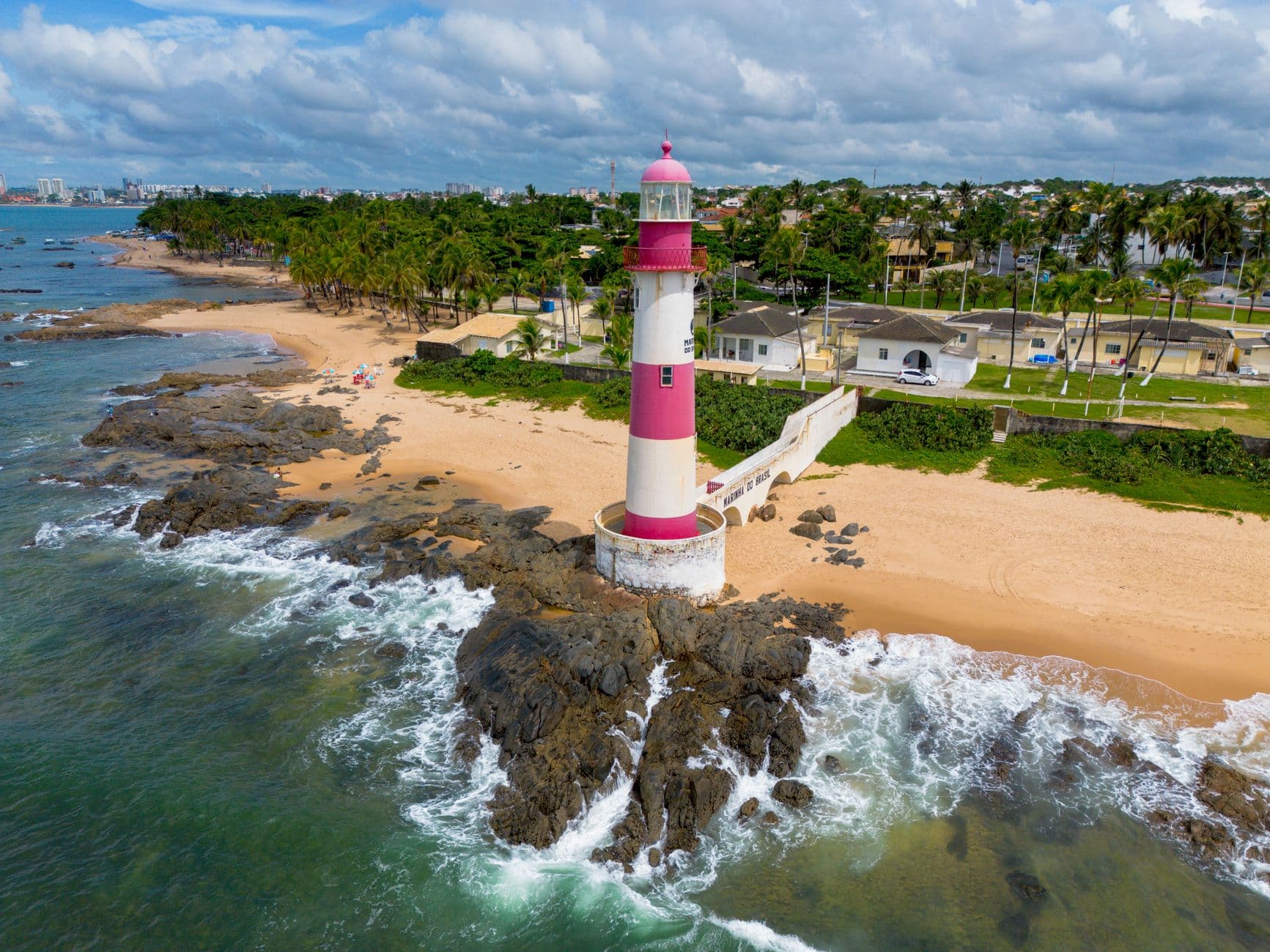 A vibrant aerial shot of the iconic Farol de Itapuã lighthouse along Salvador's coastline with lush greenery.