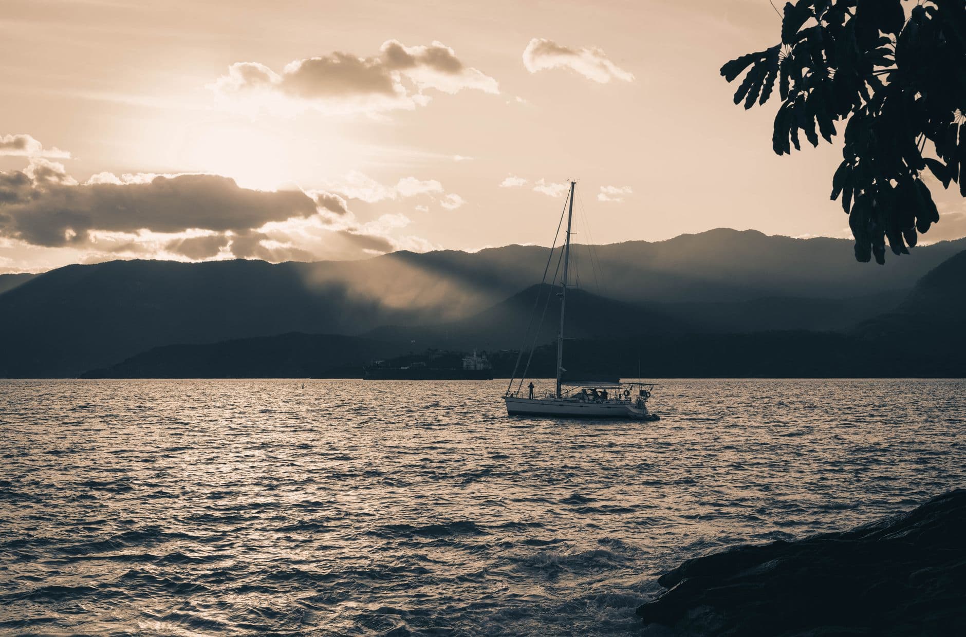A sailboat glides across the ocean at sunset with mountainous scenery in Ilhabela, Brazil.