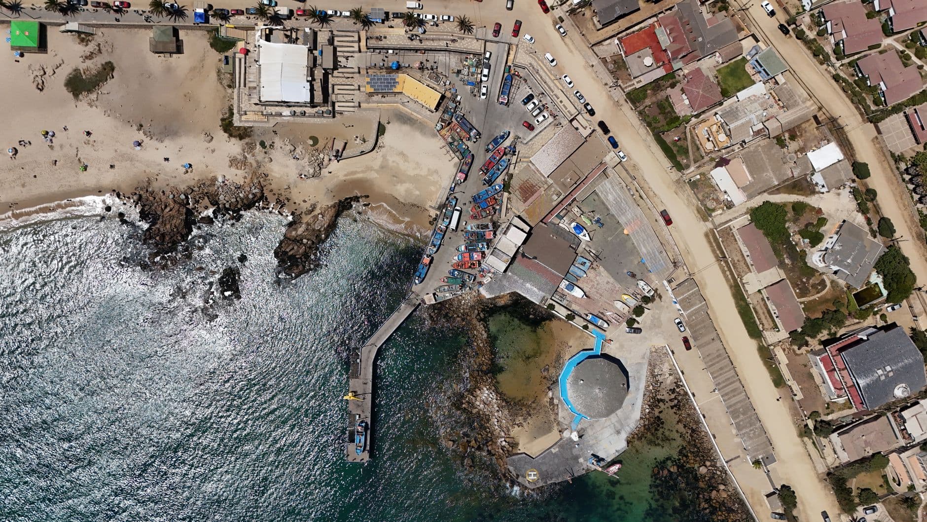 Aerial shot of a Chilean coastal village with beach, boats, and buildings.
