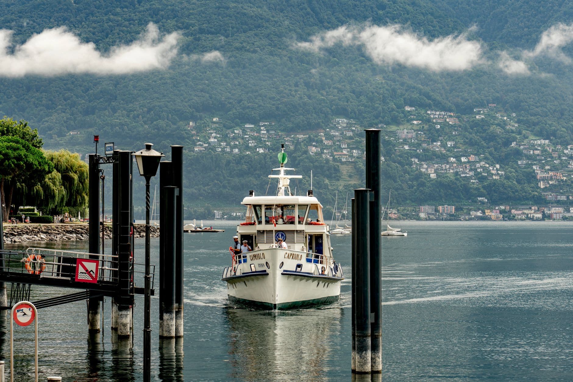 A passenger ferry approaches a dock amidst scenic green hills and cloudy sky.