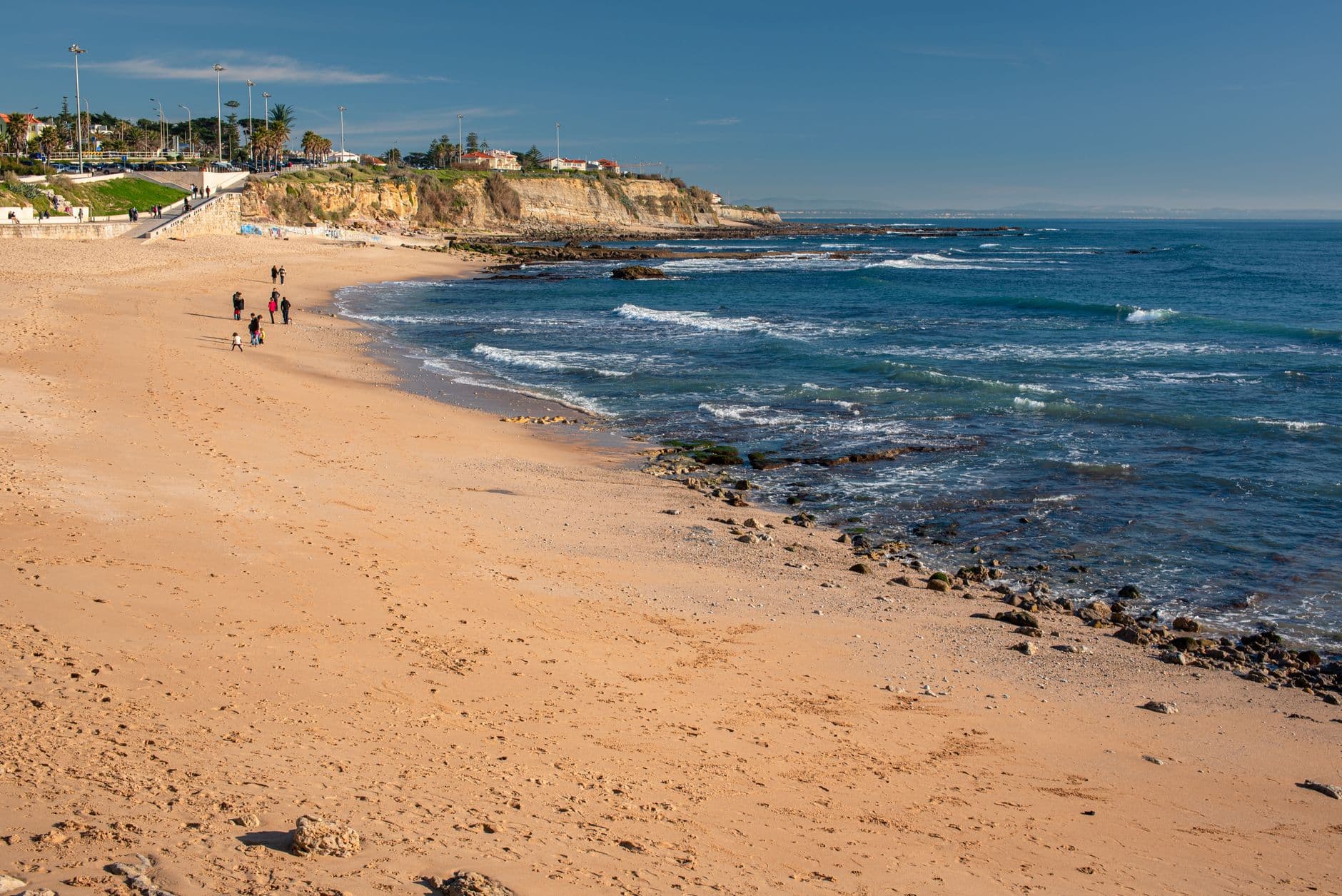 A serene sandy beach with cliffs and blue skies in Lisbon, Portugal, captured in daylight.