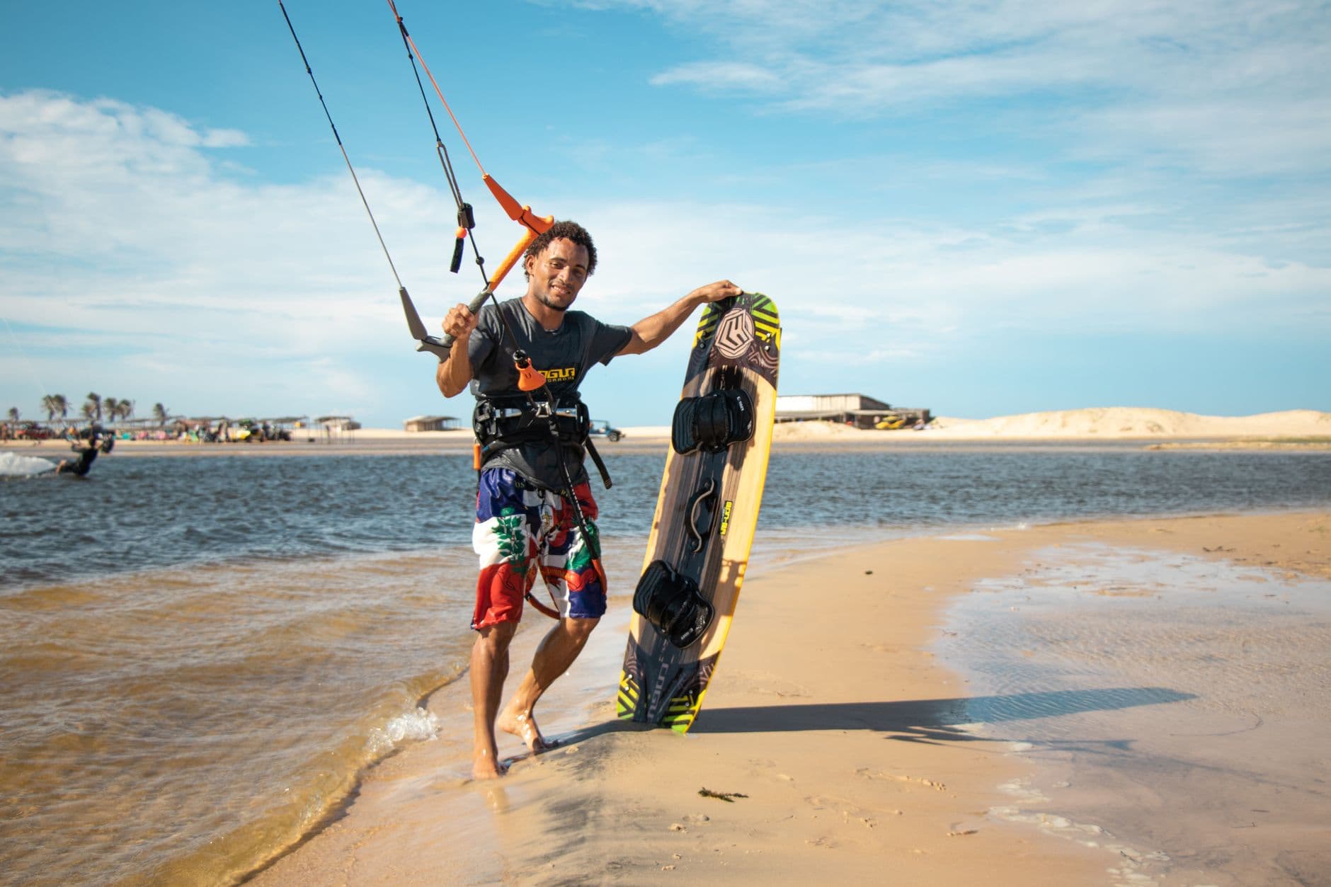 Man holding kiteboard on sunny beach, embracing sport and leisure along the sea.