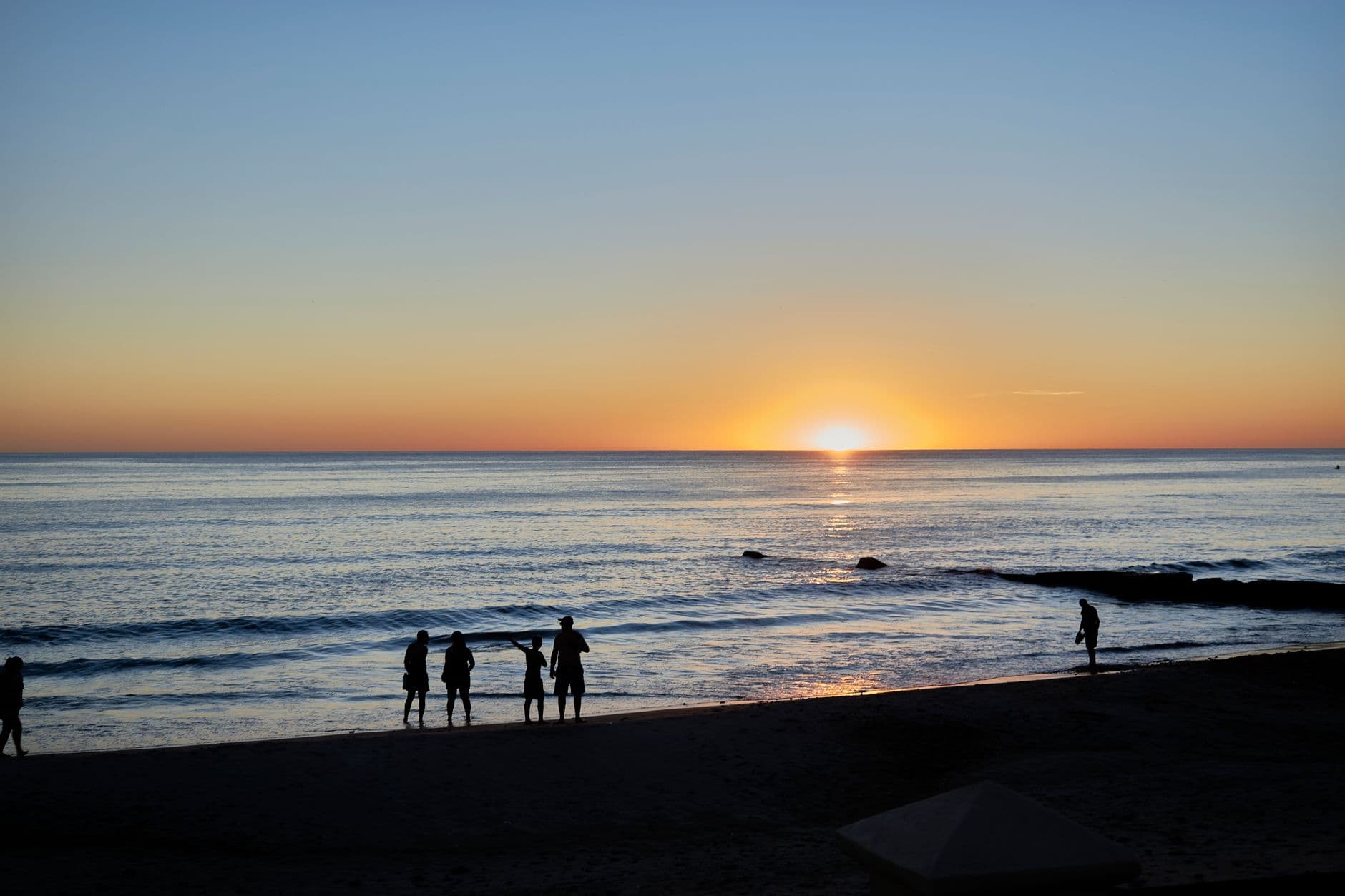 Silhouettes of people enjoying a stunning sunset over Piriápolis beach, Uruguay.