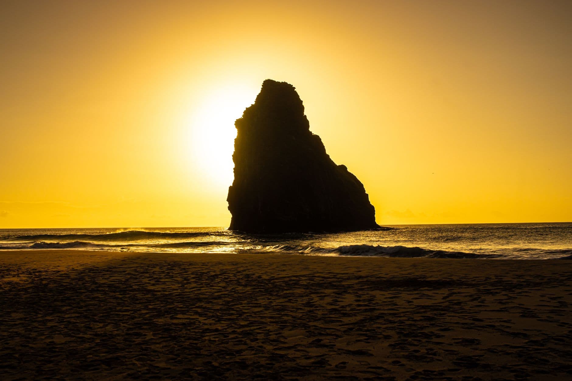 Silhouette of a rock formation on a beach during a vibrant sunset, capturing natural beauty.