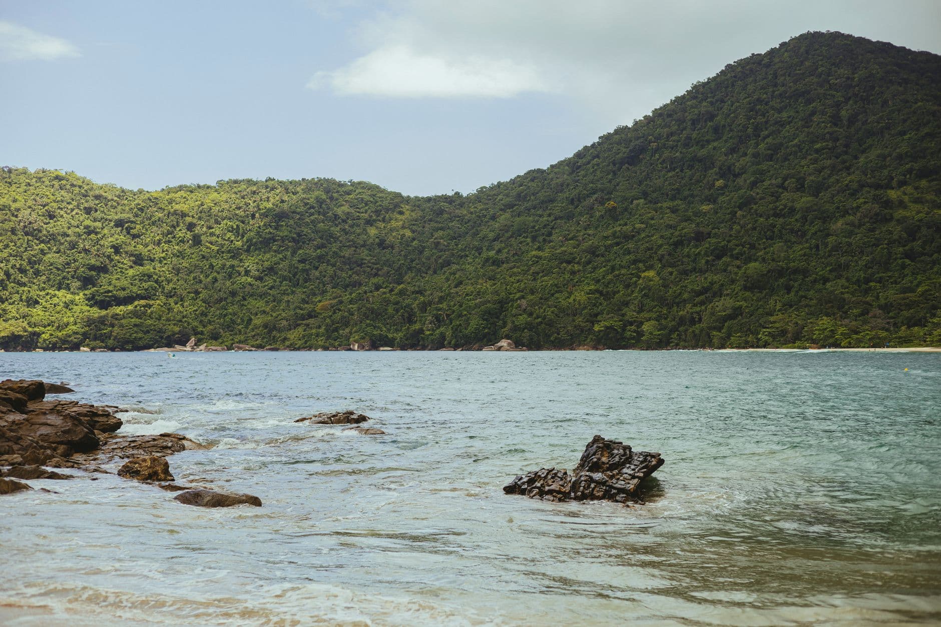 Scenic view of a serene beach surrounded by lush green hills and clear ocean waters.