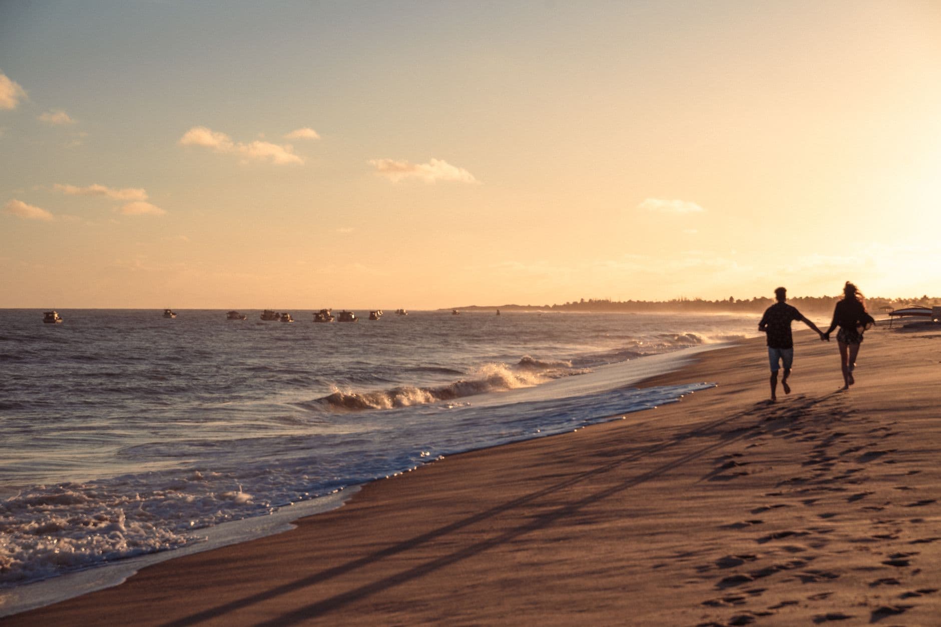 A couple holding hands and running along a Brazilian beach during a captivating sunset, capturing love and freedom.