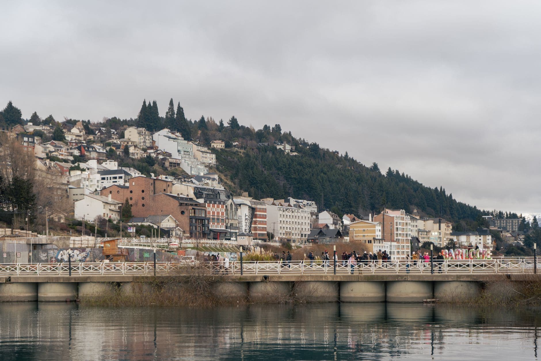 A picturesque view of Bariloche's architecture and landscape along the lake under cloudy skies.