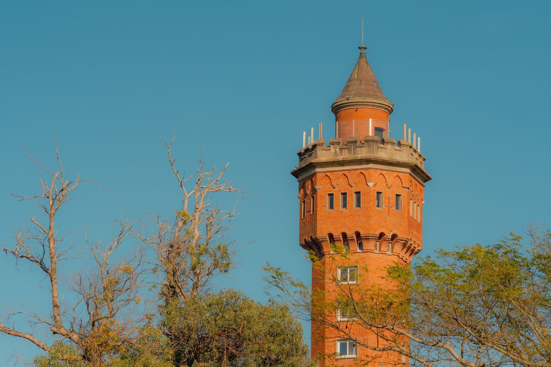 A historic brick tower in Maldonado, Uruguay, against a clear blue sky, framed by trees.