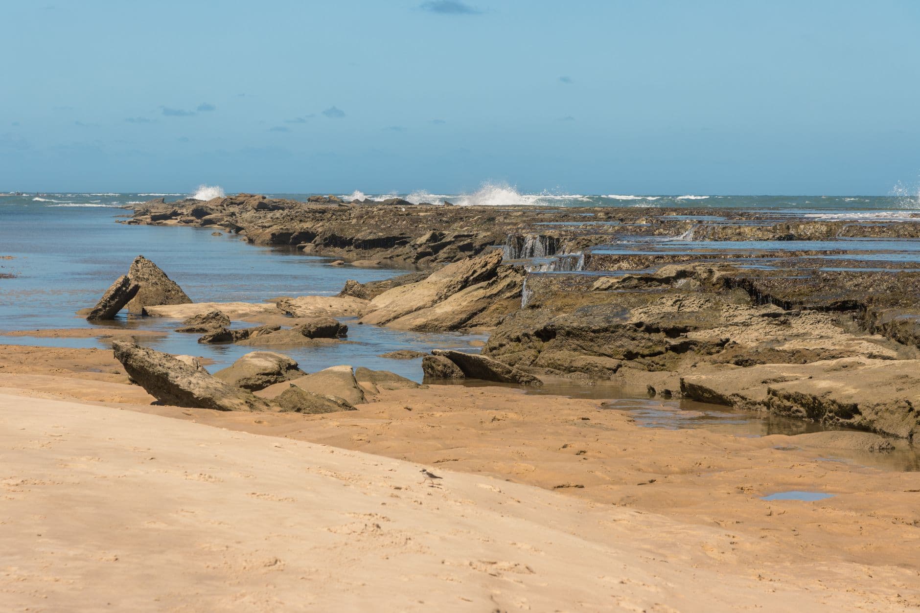 Tranquil beach scene in Natal, Brazil featuring rocky formations by the ocean under a clear blue sky.