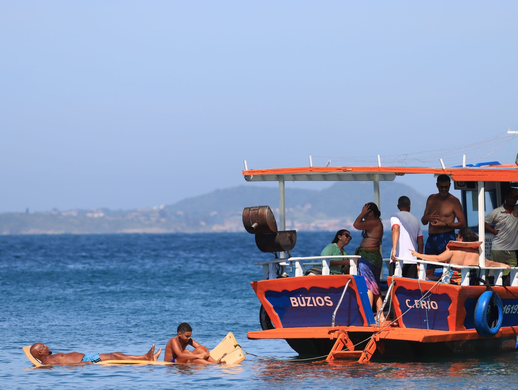 Tourists enjoying a sunny day on a Búzios boat trip, relaxing and swimming in the clear ocean waters.
