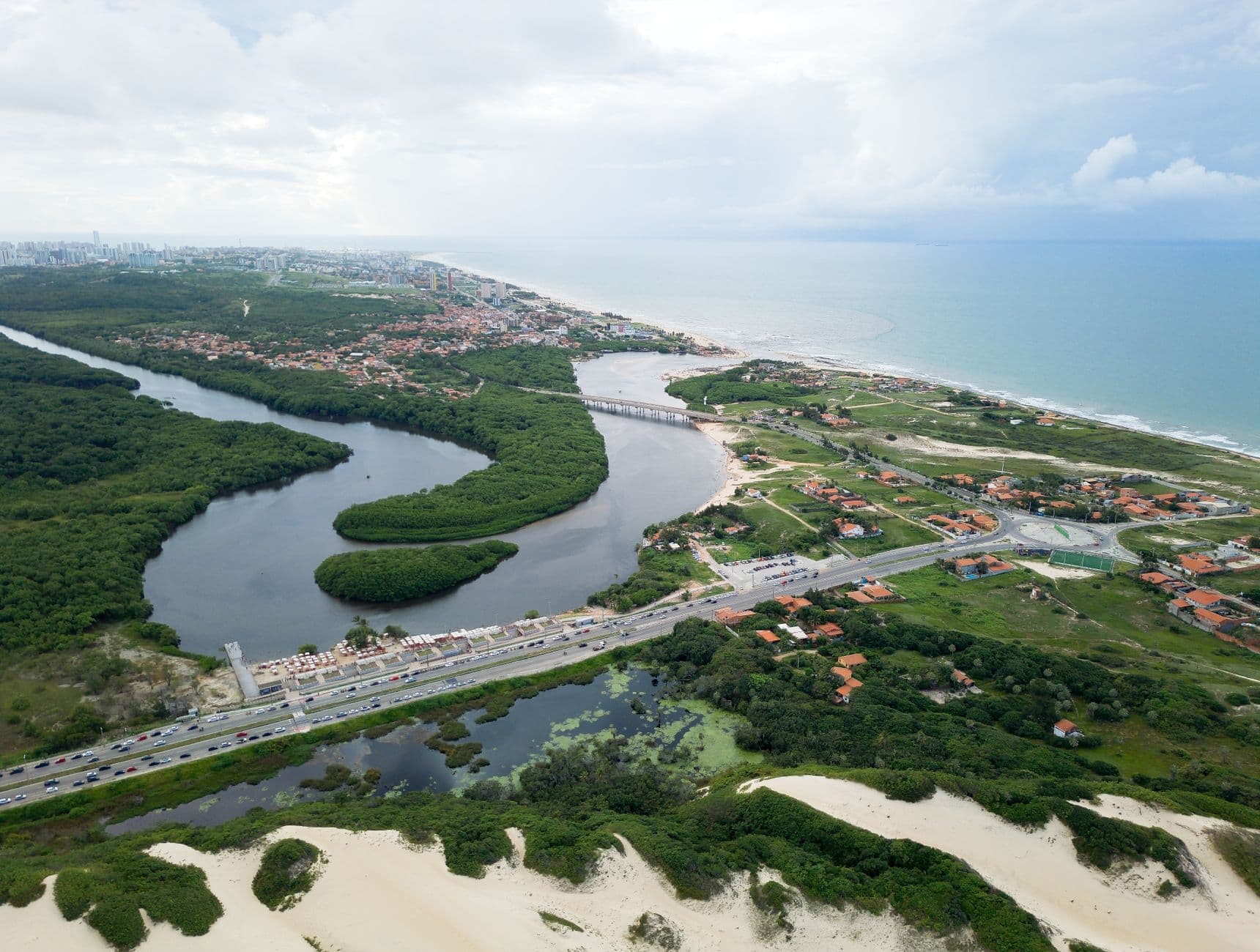 Aerial shot of Fortaleza's lush coastline, featuring winding river, dunes, and ocean.