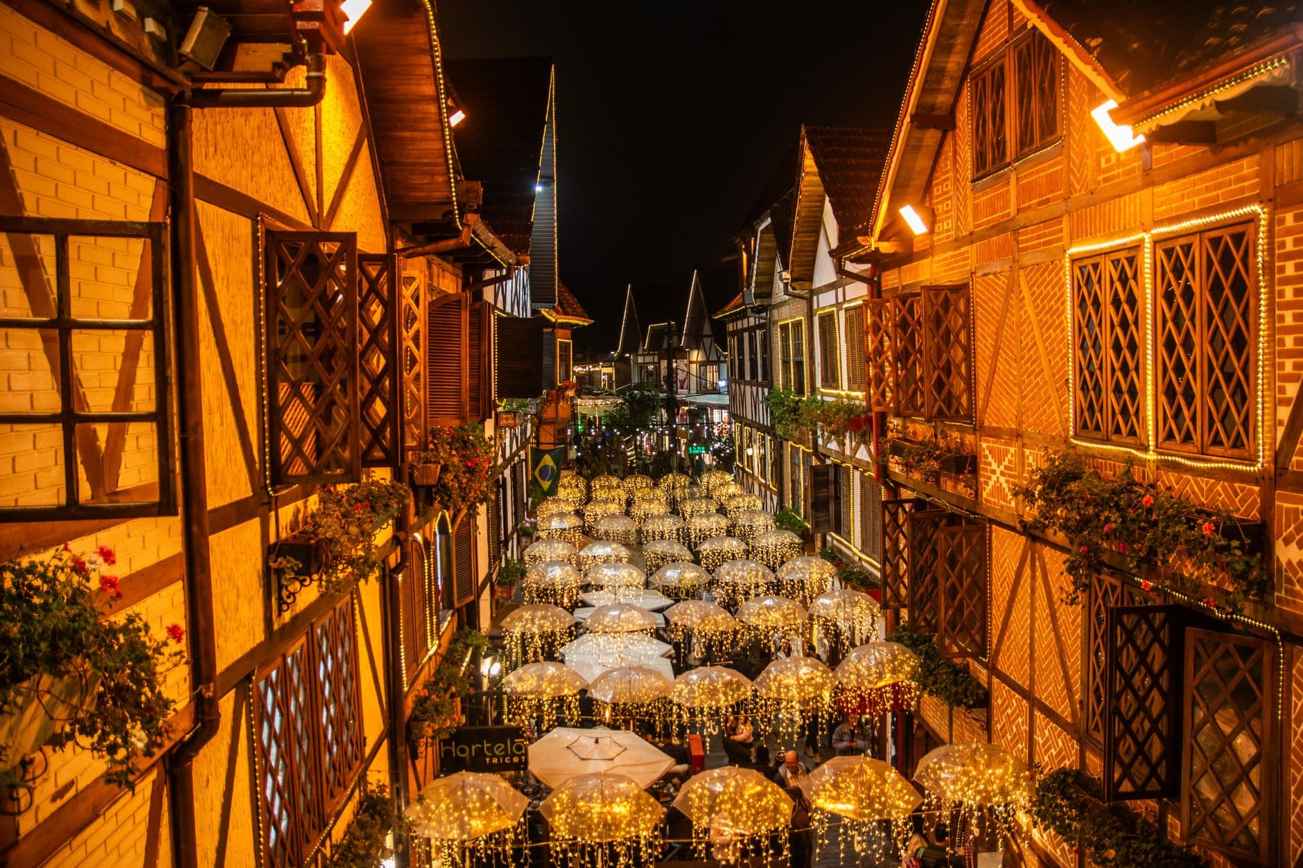 Charming European-style street in Campos do Jordão at night, adorned with festive lights and umbrellas.