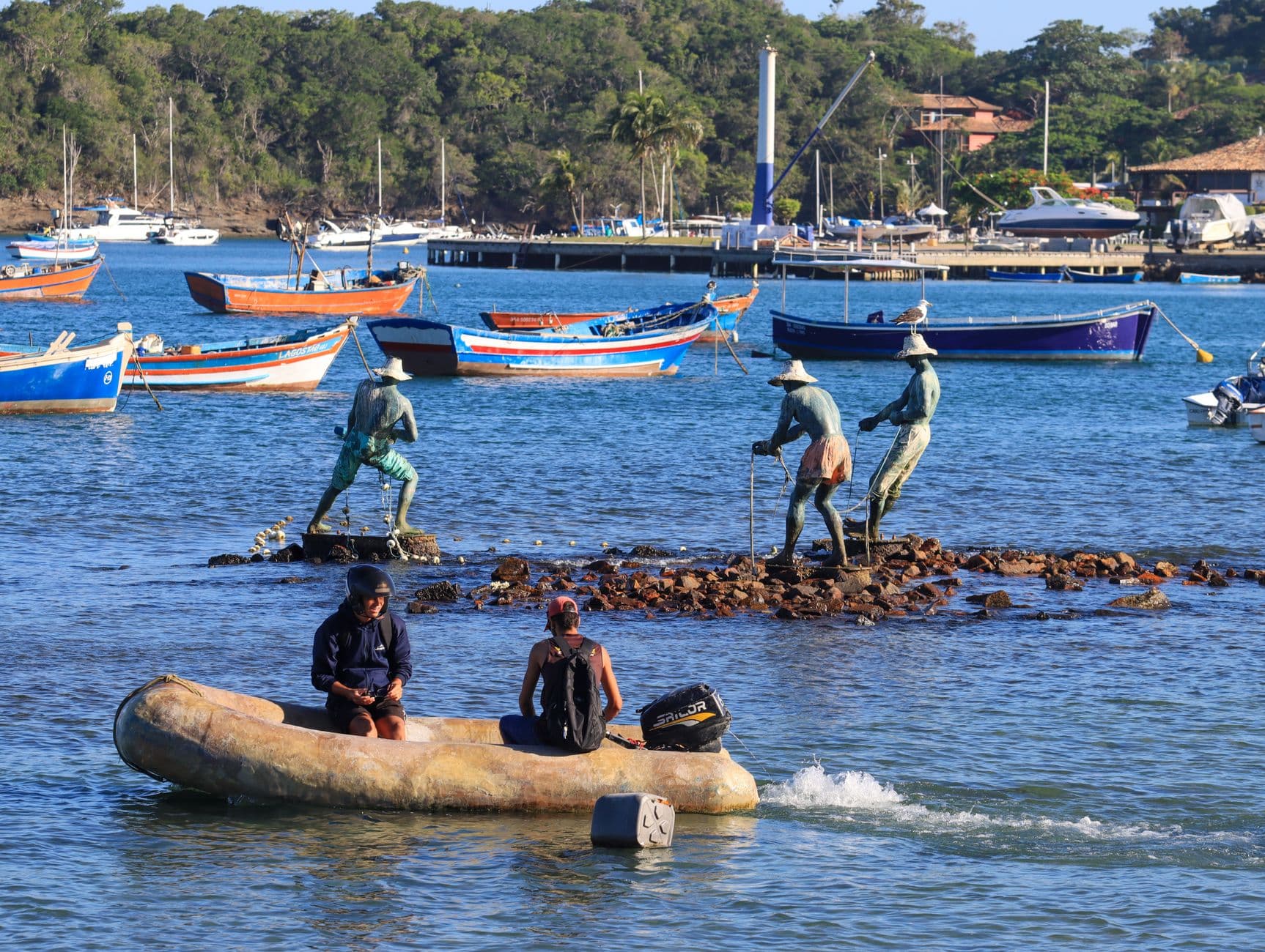 Vibrant harbor scene with fishermen statues and colorful fishing boats under clear skies.